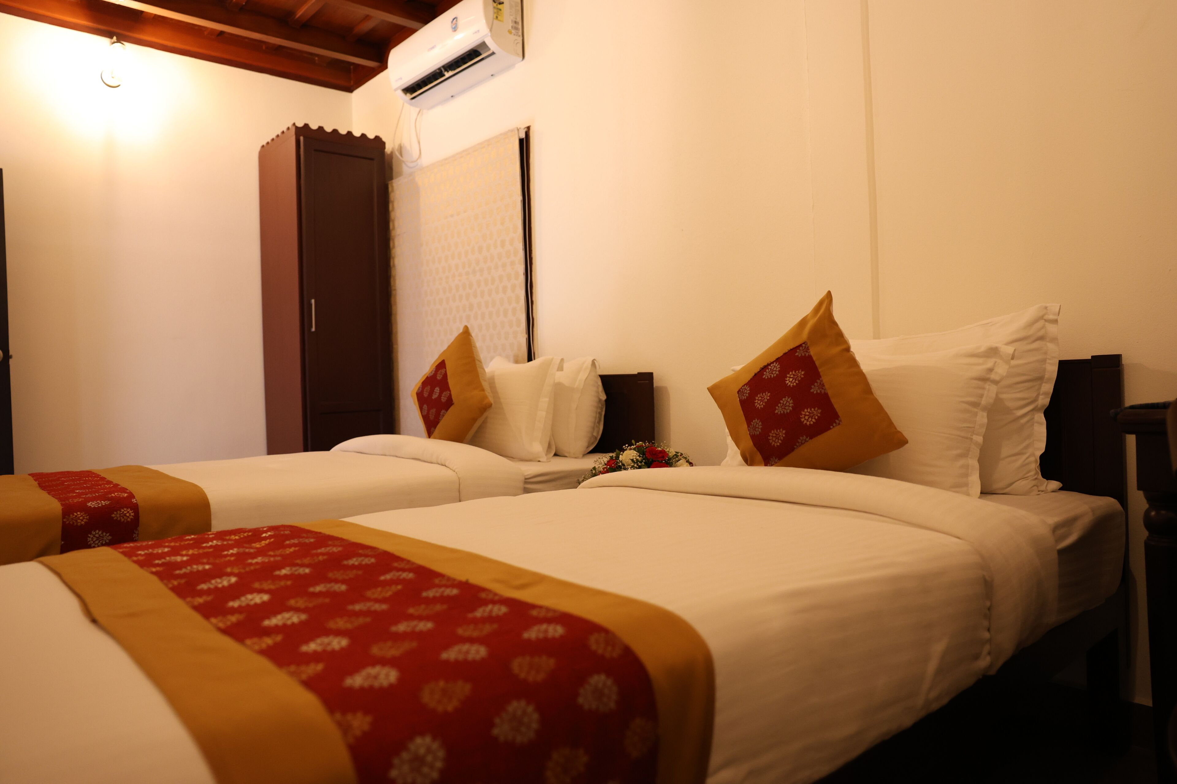 A hotel room with two beds, a wardrobe, and an air conditioning unit.