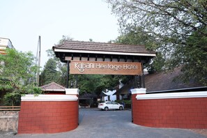 The entrance to Kabani Heritage Hotel with a sign above the entrance, a car parked in front, and a brick wall.