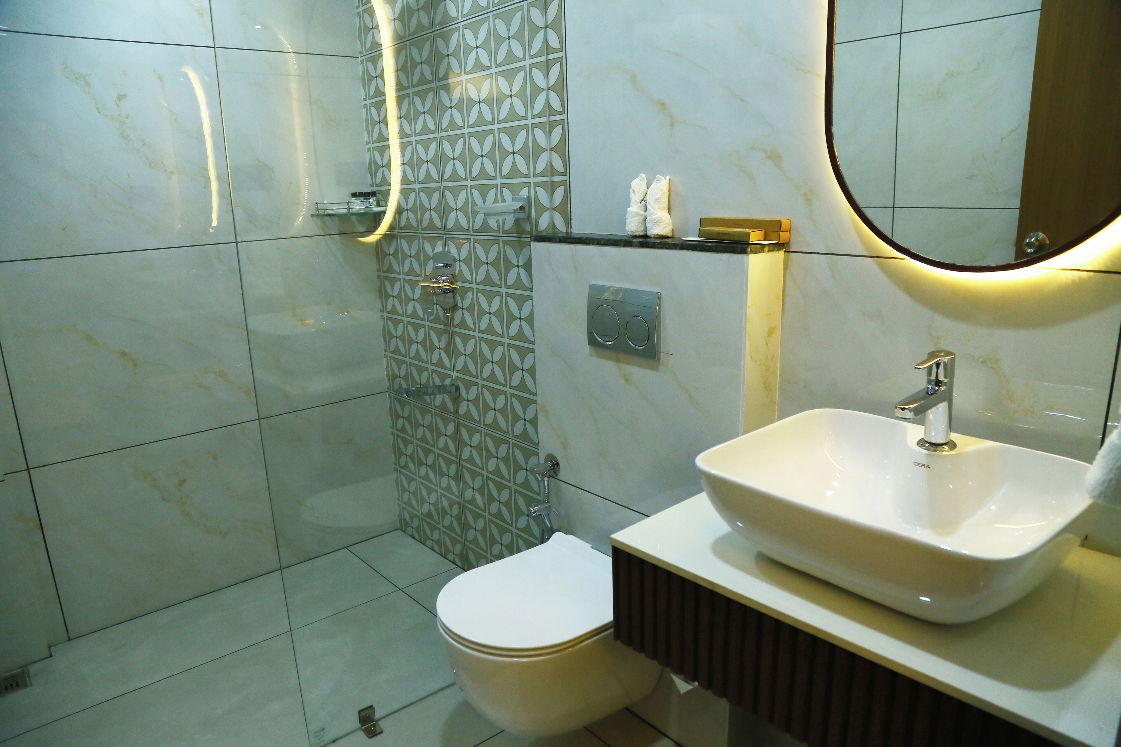 A bathroom with a toilet, a sink, a mirror, and a shower with a patterned wall.