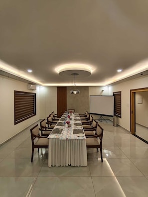 A conference room with a long table, chairs, a whiteboard, and a projector screen.