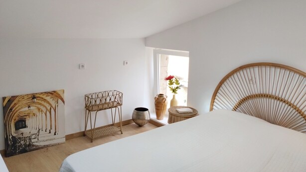 Une chambre à coucher avec un puits de lumière, un lit, une chaise, une table et un vase rempli de fleurs.