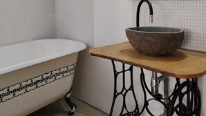 Une salle de bain avec une baignoire, un meuble-lavabo en bois avec un vasque en pierre, un miroir et une étagère avec une plante.