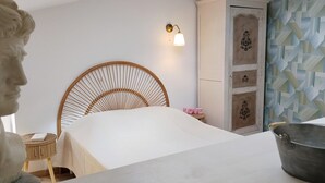 Une chambre à coucher comprenant un lit, une tête de lit en bois, une petite table de chevet, une armoire et un mur recouvert d’un papier peint à motifs géométriques.