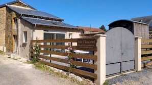 Un bâtiment rustique avec une façade en pierre, une clôture en bois et une enseigne indiquant « Gîte L’Essentiel ».