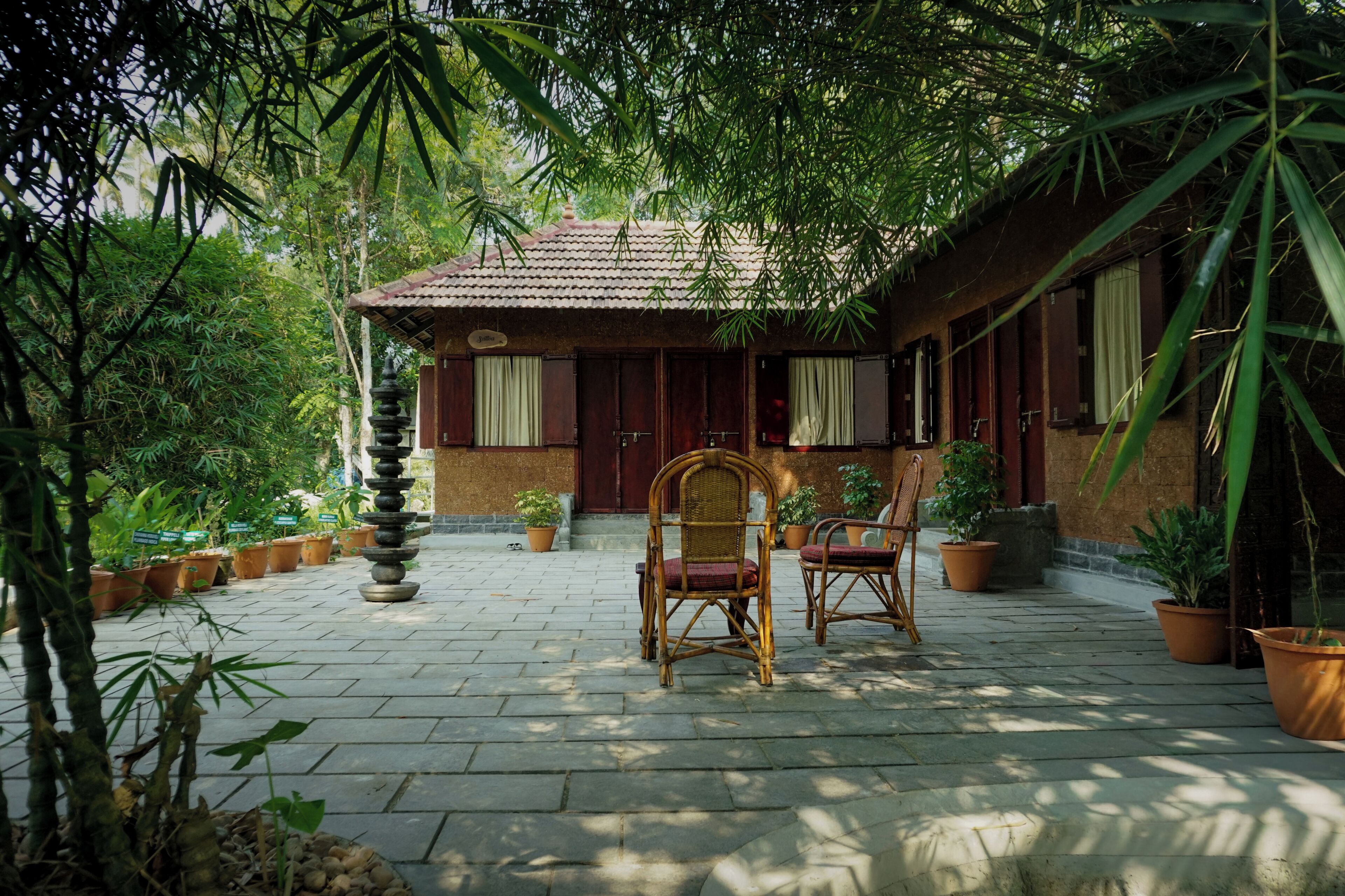 Une cour avec une maison de style traditionnel, un sol en pierre, des plantes en pot et deux chaises en osier.