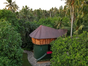 A small, green-roofed structure surrounded by lush greenery and palm trees. - THAPOVAN WATERSCAPES (Neyyattinkara)