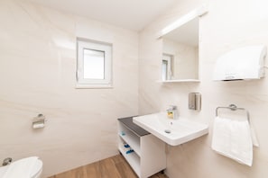 Ein Badezimmer mit einem weißen Waschbecken, einem Spiegel, einem Handtuchhalter und einem Fenster.