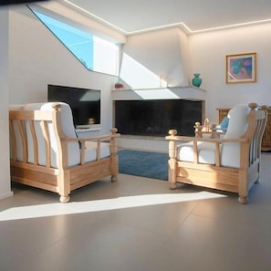 Ein modernes Wohnzimmer mit zwei Holzstühlen, einem Flachbildfernseher, einem Kamin und einem Oberlicht.