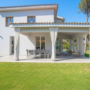 Une maison à deux étages dotée d’un patio couvert, de meubles d’extérieur et d’une pelouse bien entretenue.