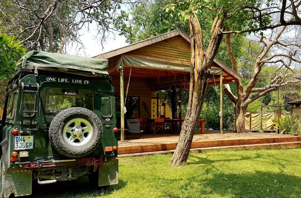 A green off-road vehicle parked in front of a covered outdoor area with a wooden deck and a building with a sloped roof.