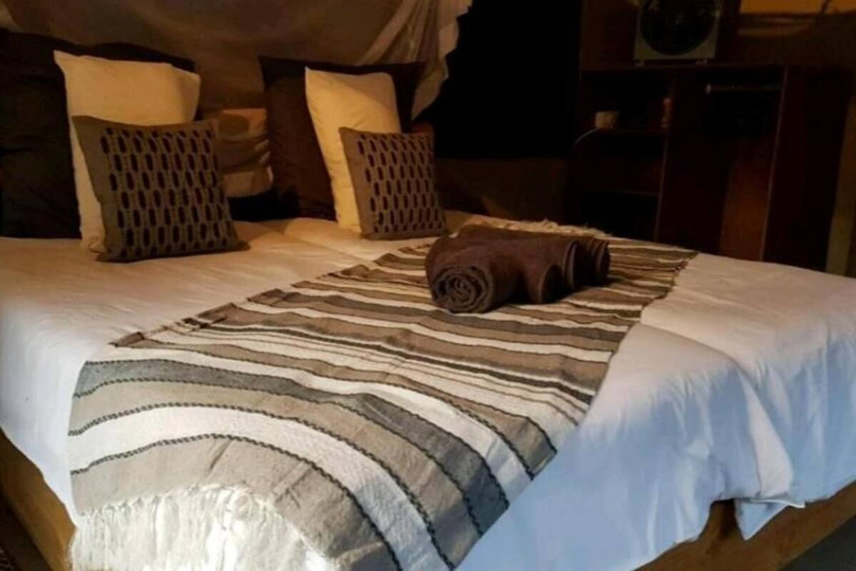 A bed with a striped blanket, multiple pillows, and a rolled towel.