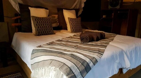 Una cama con una manta a rayas, varias almohadas y una toalla enrollada.