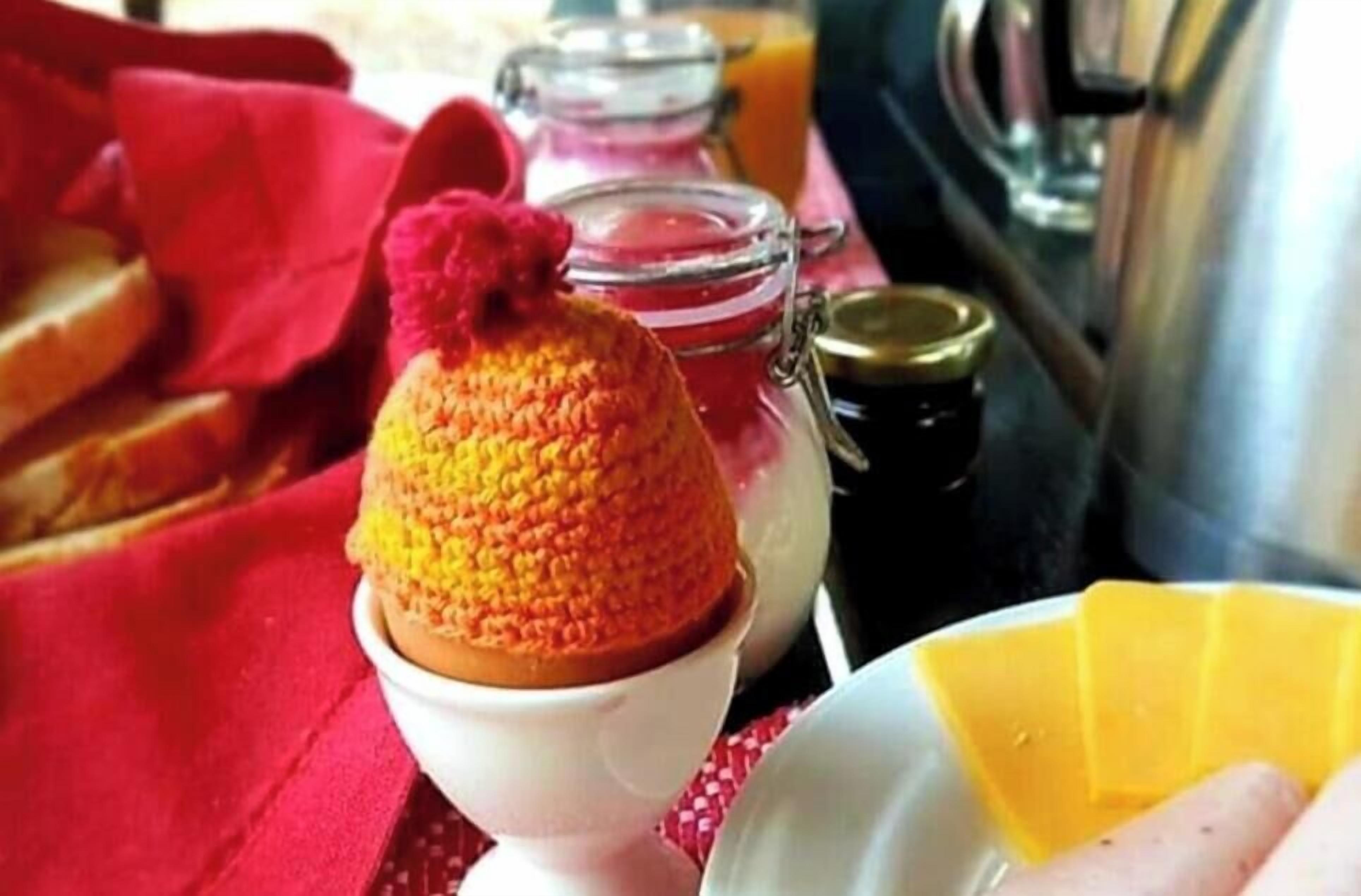 A breakfast setting with a knitted item on a white plate, a glass jar, and a metal container.