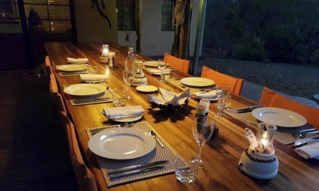 Una larga mesa de madera dispuesta para una comida, con platos, cubiertos, vasos y velas.