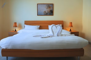 A neatly made bed with white linens, two bedside lamps, and a painting on the wall.