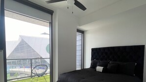 Quarto moderno com uma cama grande, um ventilador de teto e vista para um edifício através de uma janela ampla.