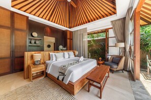 Un dormitorio moderno con techo de madera, una cama grande, mesitas de noche, una silla y vistas al exterior con vegetación.