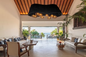Un amplio espacio habitable con vista al océano, techo de madera y una lámpara moderna.