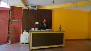 Una recepción con una persona detrás, un electrodoméstico pequeño blanco, un letrero que indica recepción de yoga y spa, y una planta en maceta.