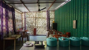 Una habitación con separador de bambú, una mesa con sillas, un ventilador de techo y una pared verde con planta trepadora.
