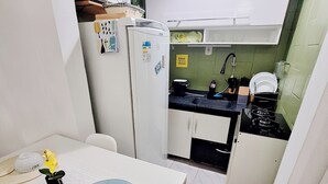 A compact kitchen with white cabinets, a microwave, a refrigerator, and a sink. There's a dining table with a placemat and a small potted plant. - Cozy●Sea View●Beach●Subway●Wi-Fi● Air Conditioning●24H Concierge●Secure (Rio de Janeiro)