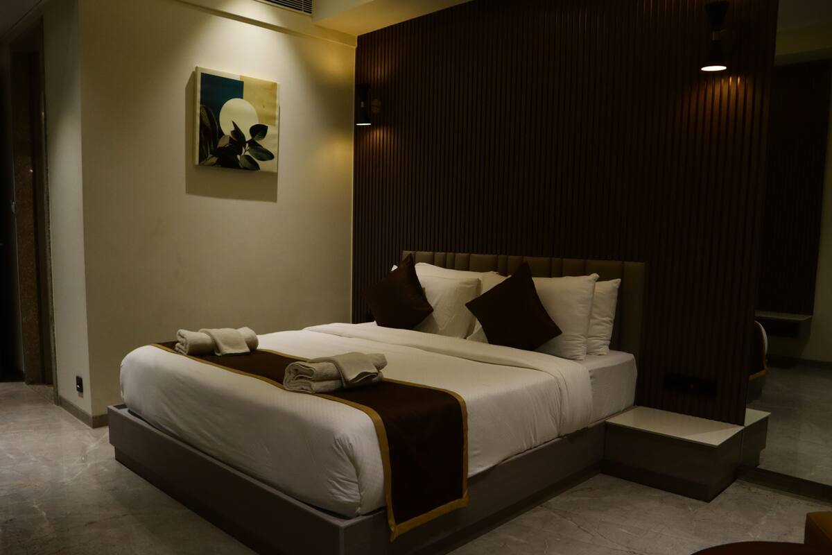 A modern hotel room with a large bed, a headboard with vertical lines, a wall-mounted artwork, and a small bedside table.