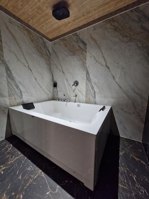 A modern bathroom with a freestanding bathtub, marble walls, and a wooden ceiling.
