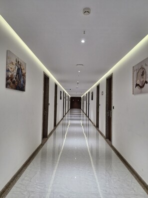 A long, well-lit hallway with marble flooring, doors on both sides, and artwork on the walls. - GREEN FUSION (Surat)