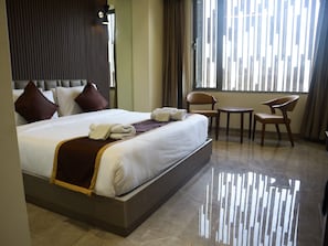 A hotel room with a large bed, a small table, two chairs, and a window with blinds. - GREEN FUSION (Surat)
