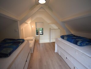 A small attic bedroom with two beds, a window, and a door leading to another room. - Seaside Escape With Large Garden (Oostkapelle)