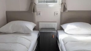 Ett sovrum med två sängar, ett litet sängbord, ett element och ett fönster med gardiner.