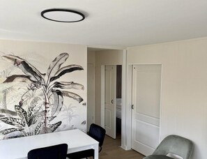 A room with a white table, two chairs, a large wall mural, and a door leading to another room. - Modern Coastal Stay in Zoutelande (Zoutelande)