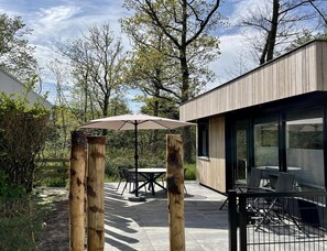 An outdoor patio with a table and chairs, a wooden post with an umbrella, and a modern building with large windows. - Modern Coastal Stay in Zoutelande (Zoutelande)