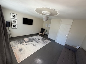 Un salon moderne avec un grand tapis, un téléviseur à écran plat, un luminaire au plafond et une porte.