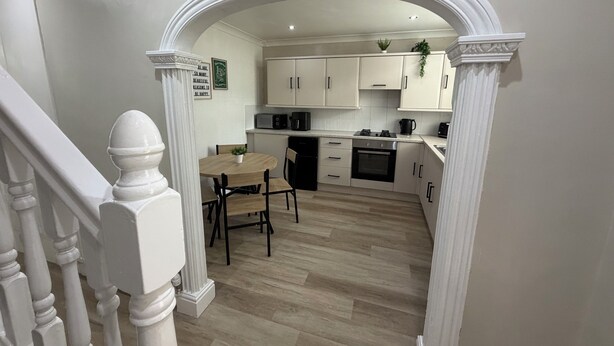 A modern kitchen with white cabinetry, a dining table, and a staircase with white balusters. - 3 bedroom house, perfect for families, groups or contractors (Liverpool)