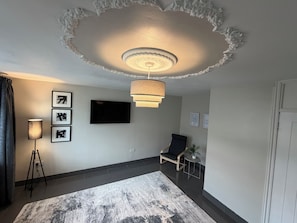 Una sala de estar moderna con un televisor de pantalla plana, una lámpara de pie, una silla y una alfombra estampada.