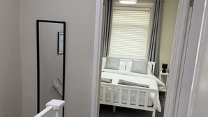 A bedroom with a bed, a bedside lamp, and a window with blinds. - 3 bedroom house, perfect for families, groups or contractors (Liverpool)