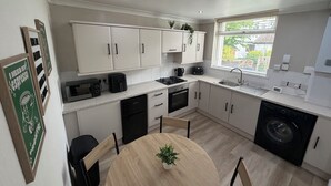 A modern kitchen with white cabinets, a round wooden table, and a built-in washing machine. - 3 bedroom house, perfect for families, groups or contractors (Liverpool)