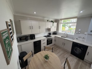 Una cocina moderna con armarios blancos, una mesa redonda de madera y una lavadora integrada.
