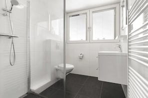 Ein modernes Badezimmer mit Duschkabine aus Glas, Toilette und Waschbecken mit weißem Unterschrank.