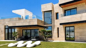 A modern two-story building with large windows, a flat roof, and a well-maintained lawn with unique white furniture. - Luxury Modern Villa with Private Pool and Rooftop Terrace (Estepona)