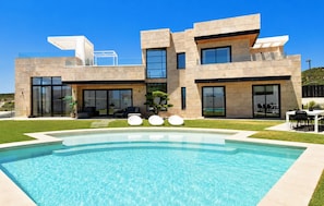 Ein modernes, zweistöckiges Haus mit Swimmingpool, großen Fenstern und einem gepflegten Rasen.