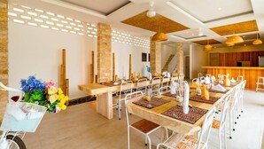 A dining area with long tables, white chairs, and a basket of flowers. - Cocotoa Boutique Hotel and Villa (Gili Trawangan)