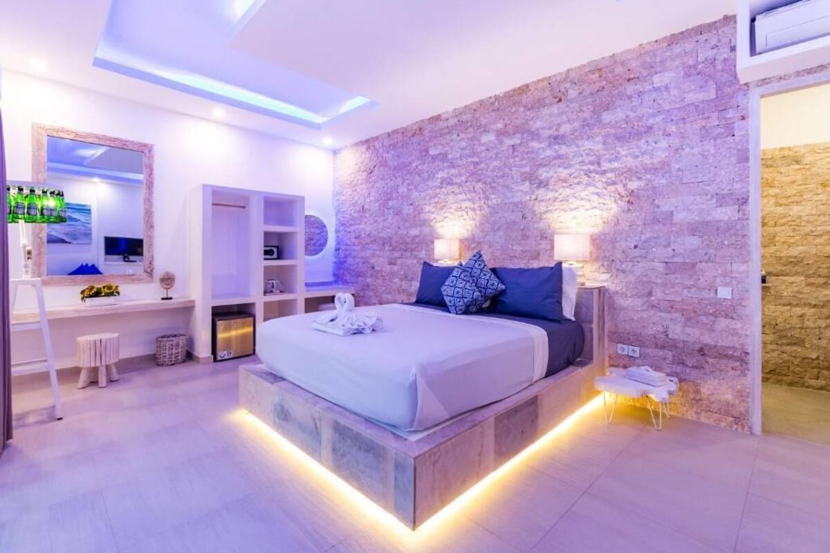 Ein modernes Schlafzimmer mit Steinwand, einem Bett mit Kopfteil, Nachttischen, einem Spiegel und einer kleinen Sitzecke.