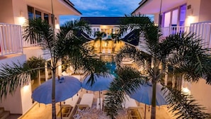 A pool area with umbrellas, palm trees, and a building with a balcony. - Cocotoa Boutique Hotel and Villa (Gili Trawangan)