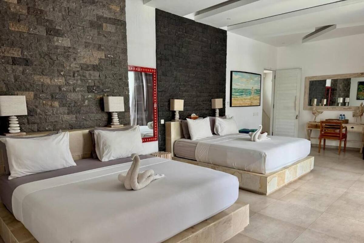 Ein Hotelzimmer mit zwei Betten, einer Steinwand, einem Gemälde, einem Schreibtisch und einem Stuhl.