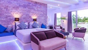 A modern bedroom with a stone wall, a large bed with patterned pillows, a sofa, and a balcony with a view. - Cocotoa Boutique Hotel and Villa (Gili Trawangan)