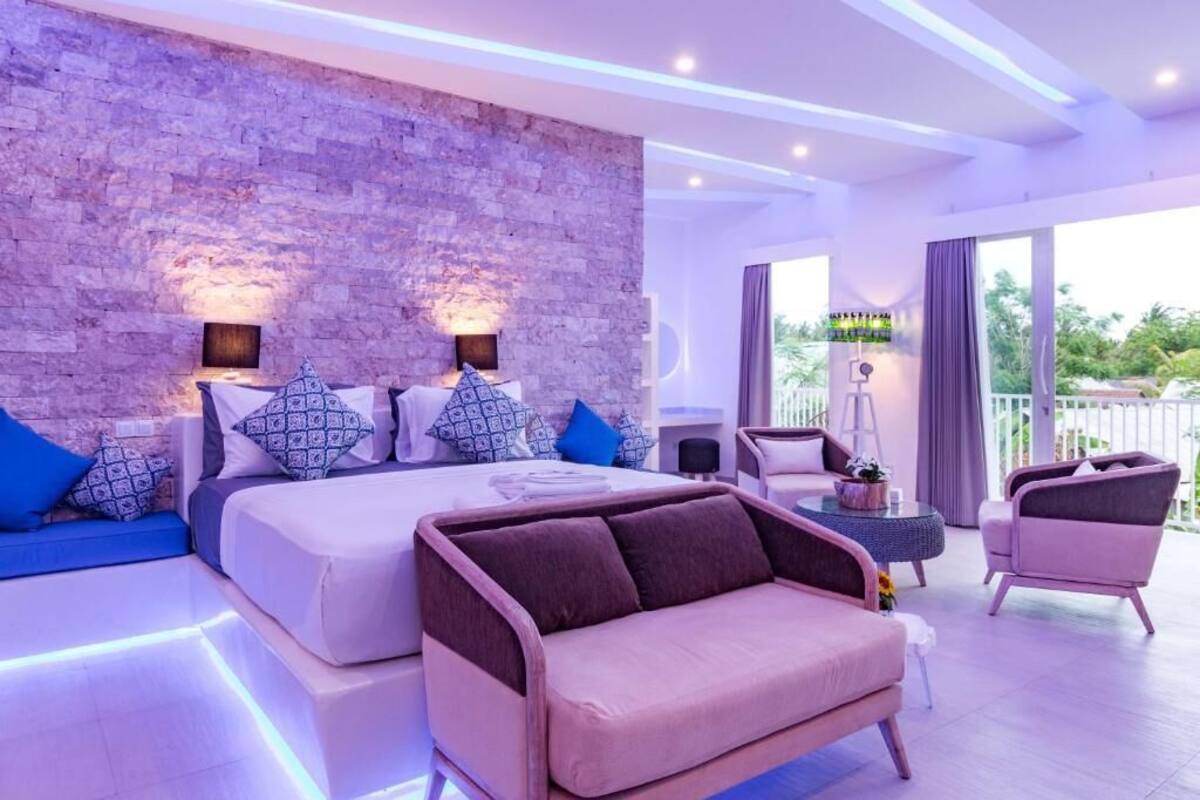 Ein modernes Schlafzimmer mit Steinwand, einem großen Bett mit gemusterten Kissen, einer Couch und einem Balkon mit Aussicht.