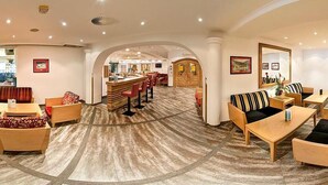 Un hall de hotel espacioso con una zona de bar central, diversas opciones de asientos y vistas al salón de comidas.
