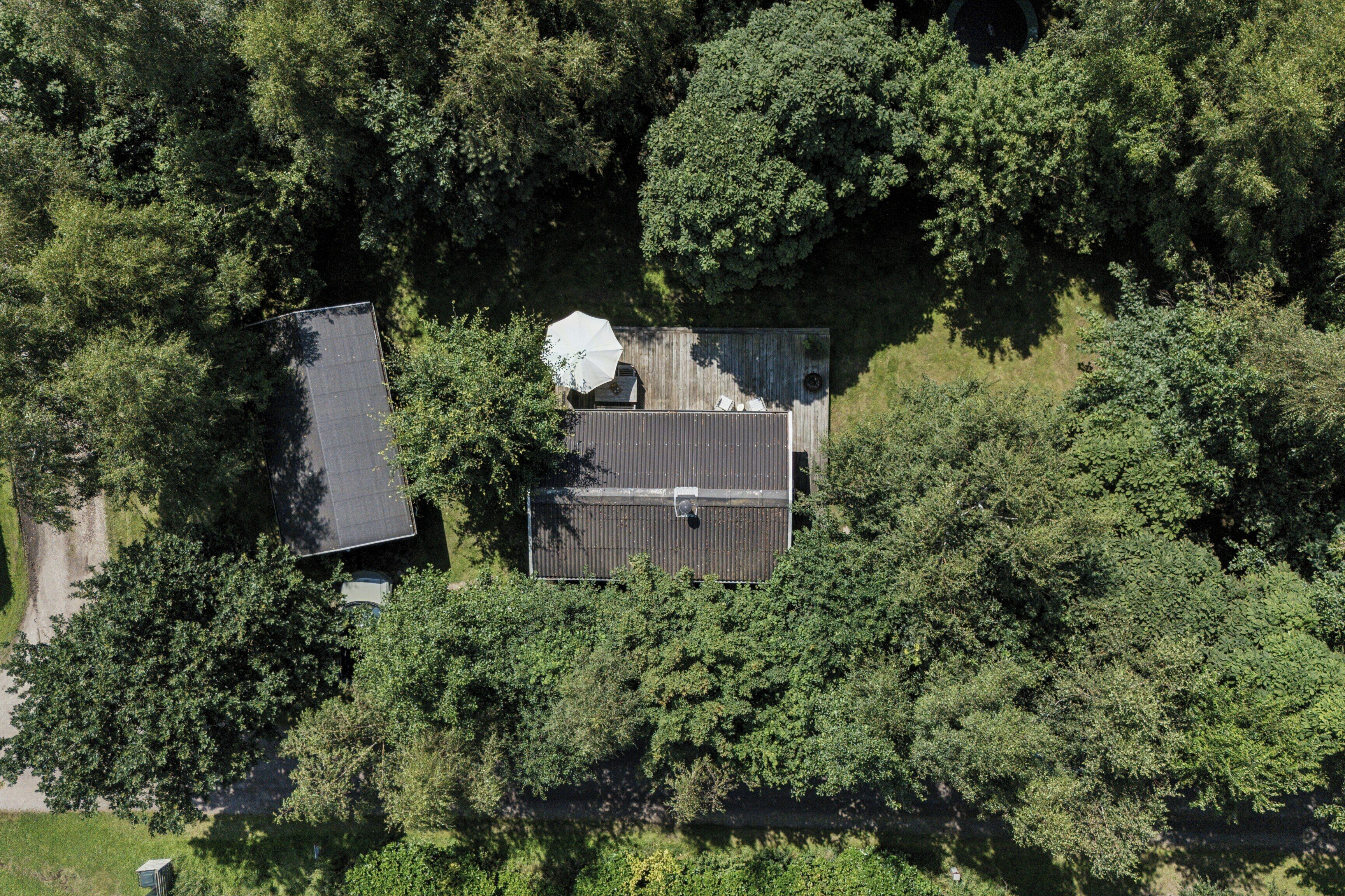 An aerial view of a property surrounded by dense trees, featuring a building with a flat roof and a visible satellite dish.